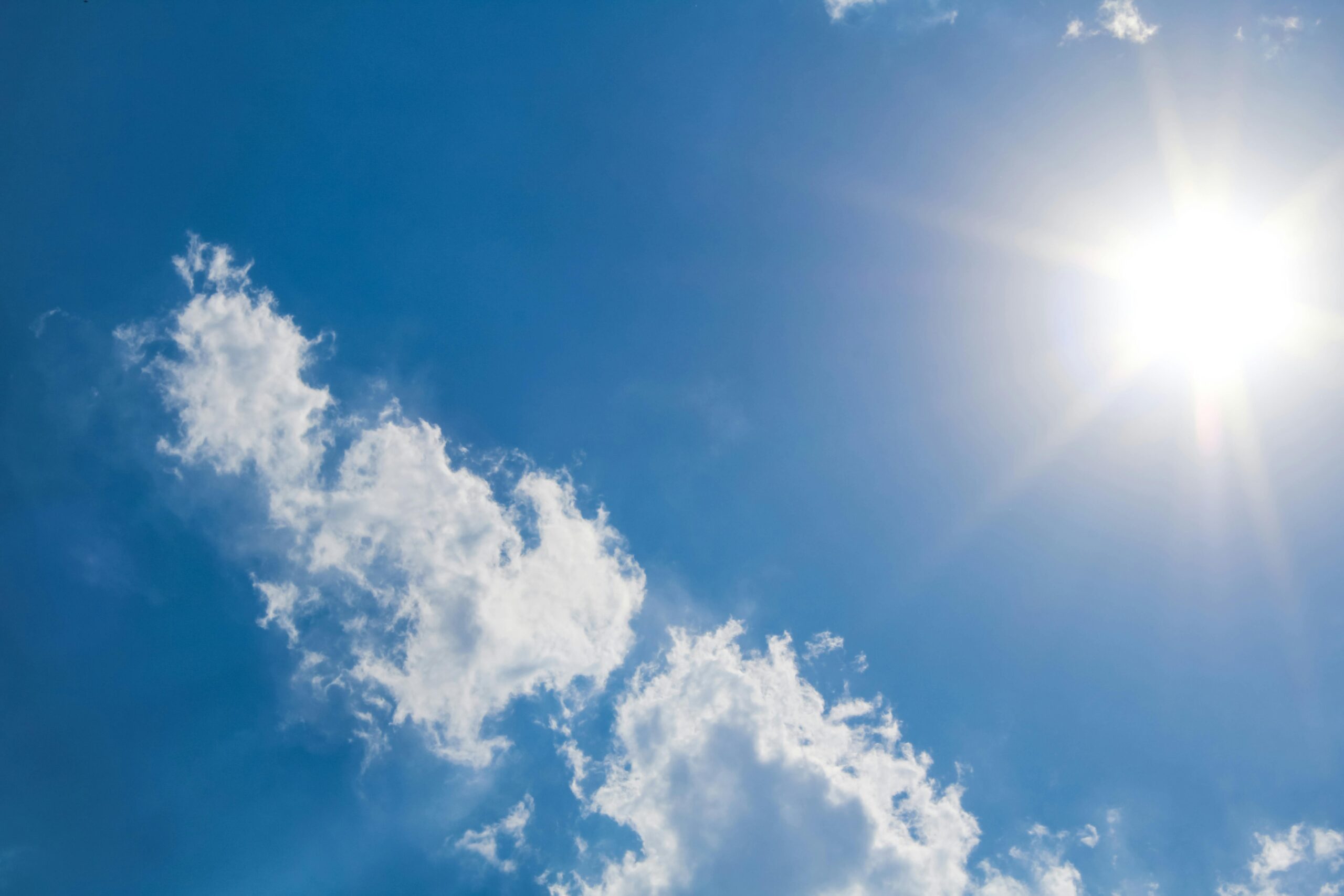 A clear blue sky with fluffy clouds and bright sunshine, representing a perfect summer day.